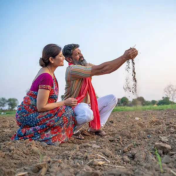 Two farmers crouched in a turned field, letting fresh soil run through their hands.